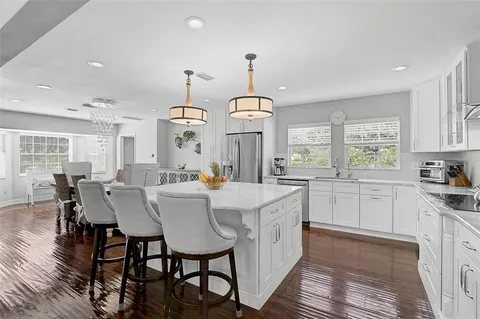 a kitchen with stainless steel appliances granite countertop a refrigerator a sink dishwasher a stove and white cabinets with wooden floor