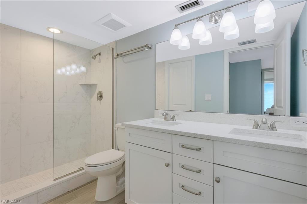 5 Bluebill Avenue, Unit 210 Naples, FL 34108 - Photo 14 of 26 a bathroom with a toilet a sink a mirror a vanity and shower