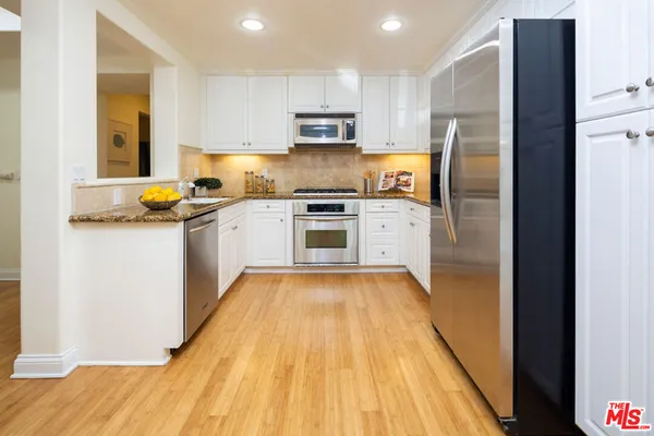 a kitchen with granite countertop wooden floors stainless steel appliances and a counter space