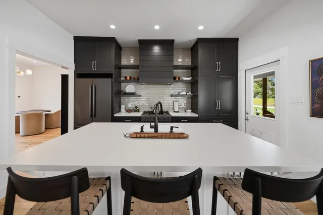 a kitchen with stainless steel appliances kitchen island granite countertop a dining table chairs and a refrigerator