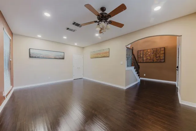 a view of an empty room with wooden floor and a ceiling fan