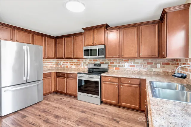 a kitchen with granite countertop wooden cabinets a stove a sink and a refrigerator with wooden floor