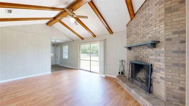 a view of an empty room with wooden floor fireplace and a window