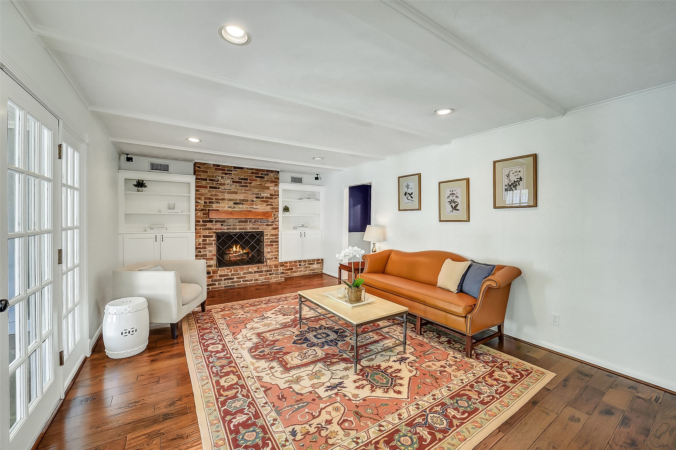 10026 Overbrook Lane Houston, TX 77042 - Photo 11 of 29 Spacious family room anchored by a brick-surround fireplace, flanked by custom built-in shelving & cabinetry for both storage and display. Beamed ceiling, recessed lighting, and mounted ceiling speakers elevate the space, while hardwood flooring adds warmth and continuity throughout.