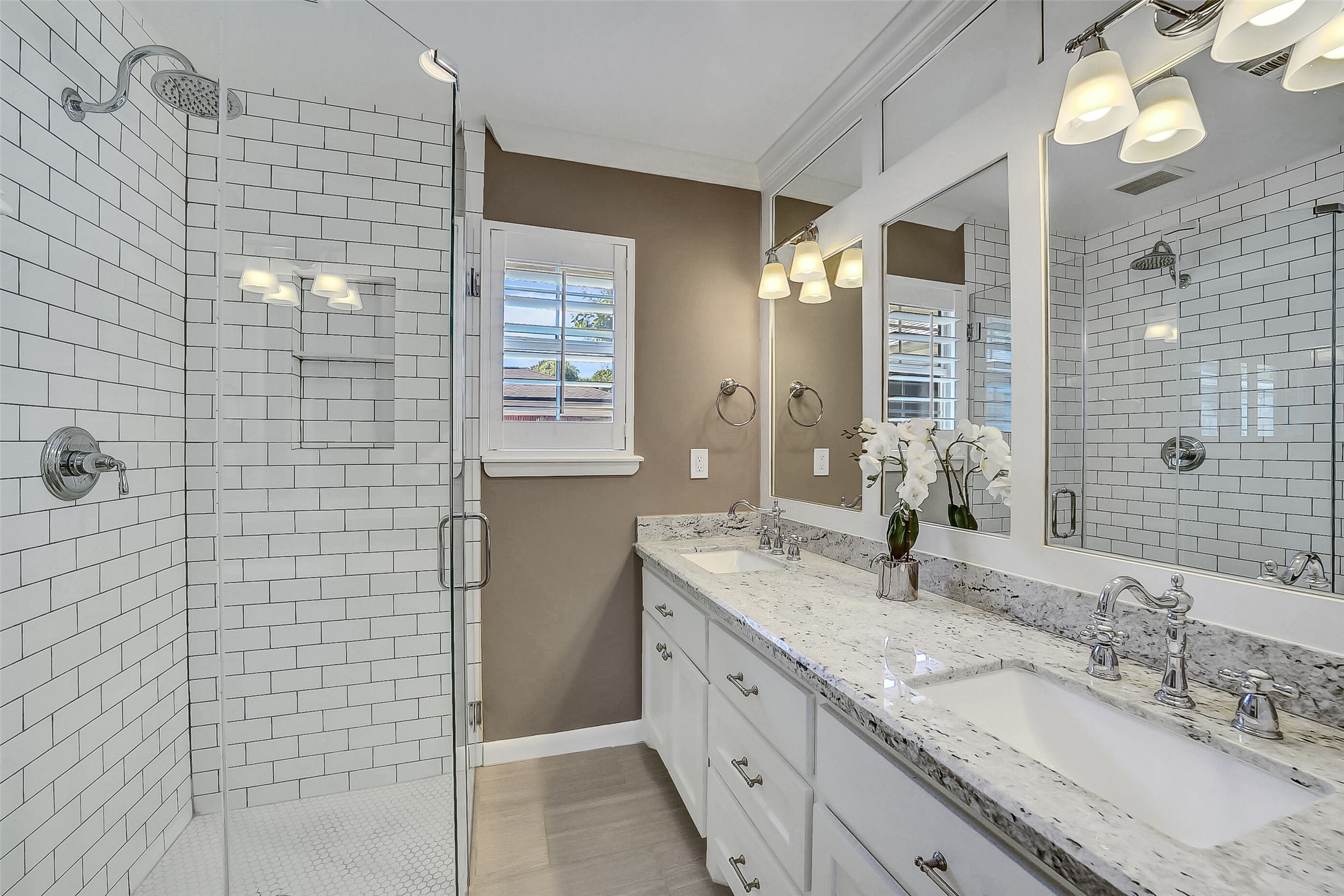 10026 Overbrook Lane Houston, TX 77042 - Photo 19 of 29 Updated primary bath features a granite-toppe vanity w/ dual sinks, built-in mirrors and decorative sconces. Window w/ plantation shutters brings in natural light, while the shower showcases a glass enclosure, subway tile surround, and hexagon tile flooring.