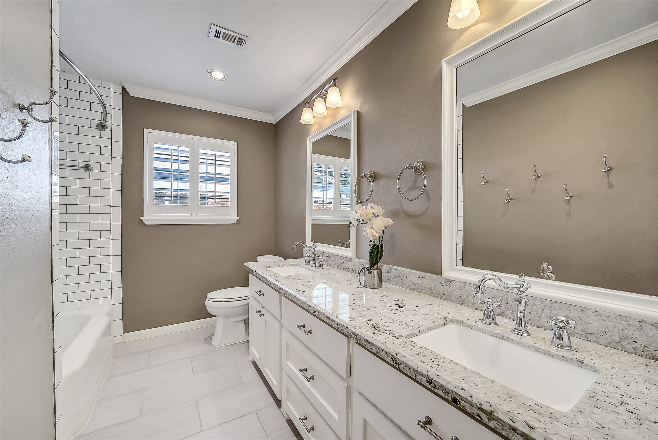 10026 Overbrook Lane Houston, TX 77042 - Photo 22 of 29 Renovated secondary bath features a granite-topped dual vanity w/ ample counter space and storage below. Tub/shower combination w/ subway tile surround and tile flooring, complemented by recessed lighting and crown molding. Plantation shutters provide natural light, while built-in mirrors w/ decorative sconces and additional storage w/ hamper add both function and style.