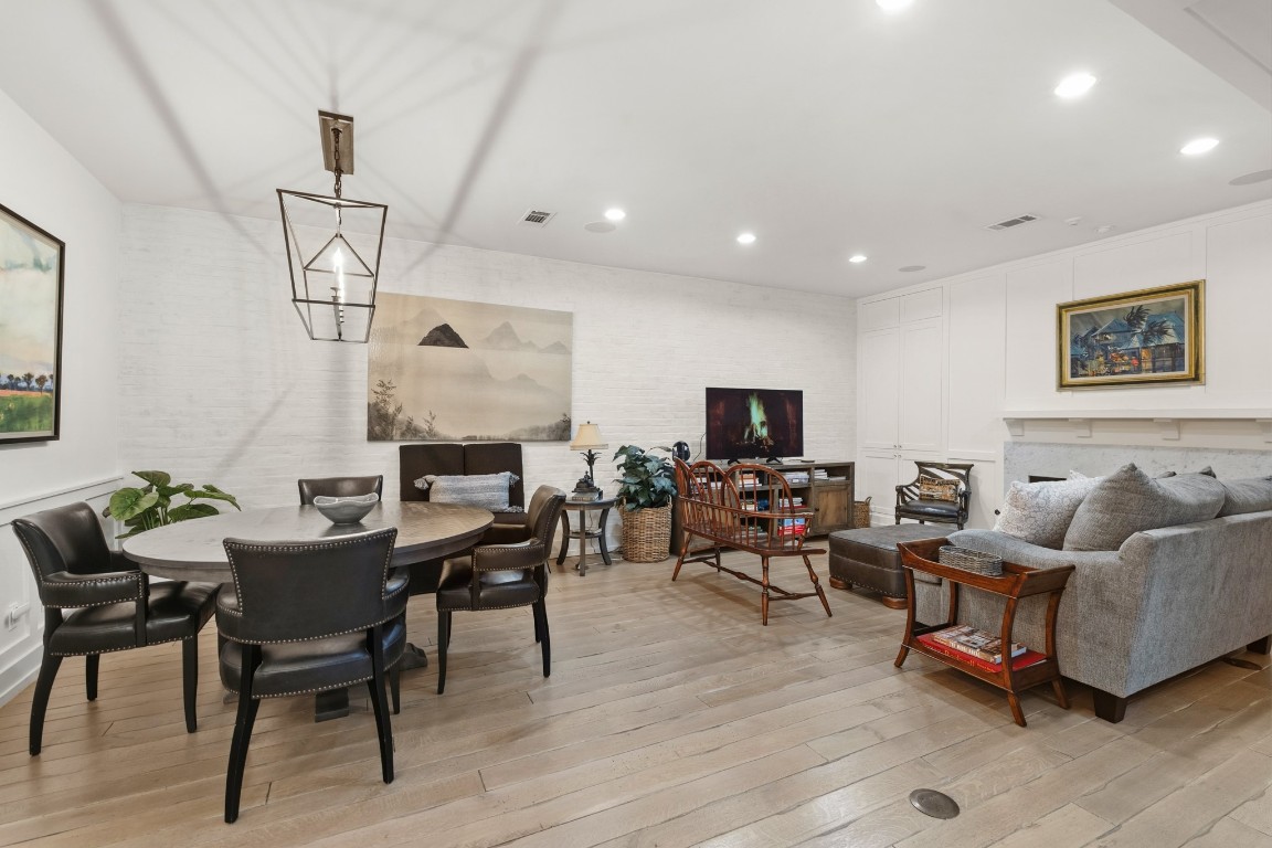 7606 Del Monte Drive Houston, TX 77063 - Photo 9 of 19 This inviting living space features a cozy seating area with a gray sofa, a round dining table with leather chairs, and modern art pieces. Hardwood floors and white walls enhance the bright, open feel, complemented by recessed lighting and a contemporary chandelier.