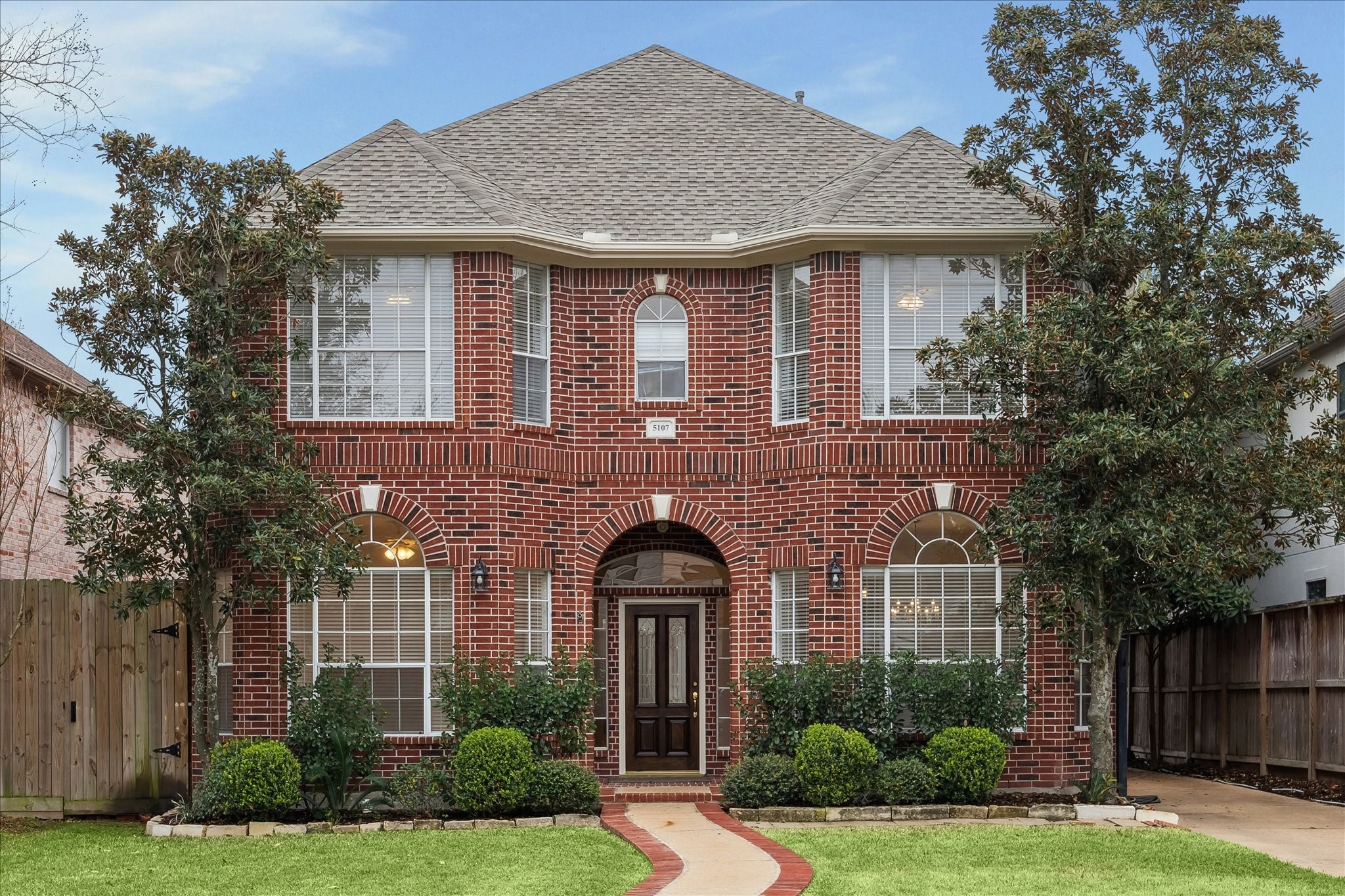 5107 Locust Street Bellaire, TX 77401 - Photo 1 of 45 Welcome to 5107 Locust St in Bellaire, featuring a classic two-story brick exterior with arched window accents, a covered entry with a beautiful front door flanked by windows, & manicured landscaping enhancing curb appeal.