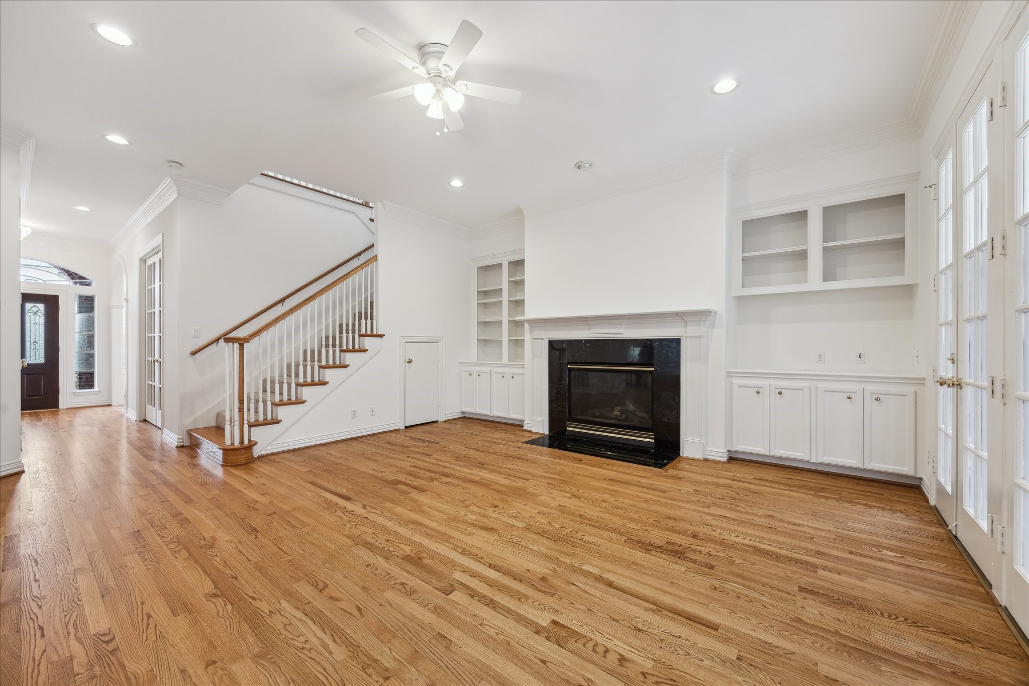5107 Locust Street Bellaire, TX 77401 - Photo 13 of 45 Additional view of the family room highlighting hardwood floors, a classic fireplace with custom built-ins, crown molding, & recessed lighting. The open layout and elegant architectural details create a sophisticated yet comfortable setting.