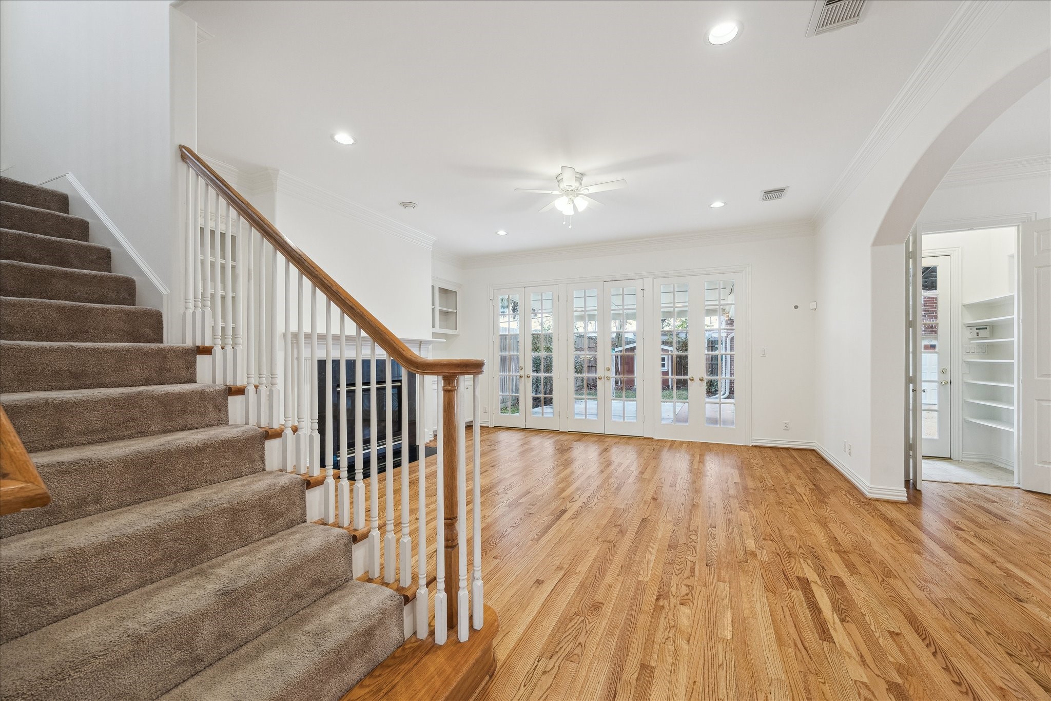 5107 Locust Street Bellaire, TX 77401 - Photo 15 of 45 View of the family room highlighting hardwood floors, crown molding, recessed lighting, & a graceful staircase with wood handrail and white balusters, creating a bright, refined setting that anchors the main living level.