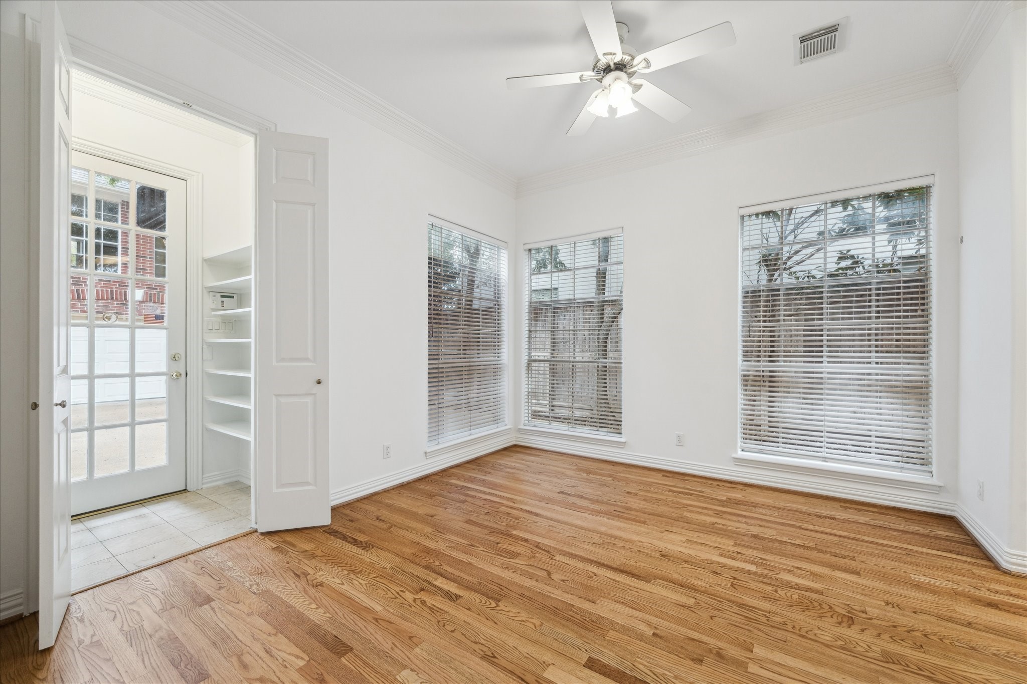 5107 Locust Street Bellaire, TX 77401 - Photo 18 of 45 Sunlit breakfast room featuring hardwood floors, crown molding, & walls of windows that create an airy, inviting atmosphere. Conveniently located off the kitchen with easy access to the covered patio through the mudroom with built-in shelving.