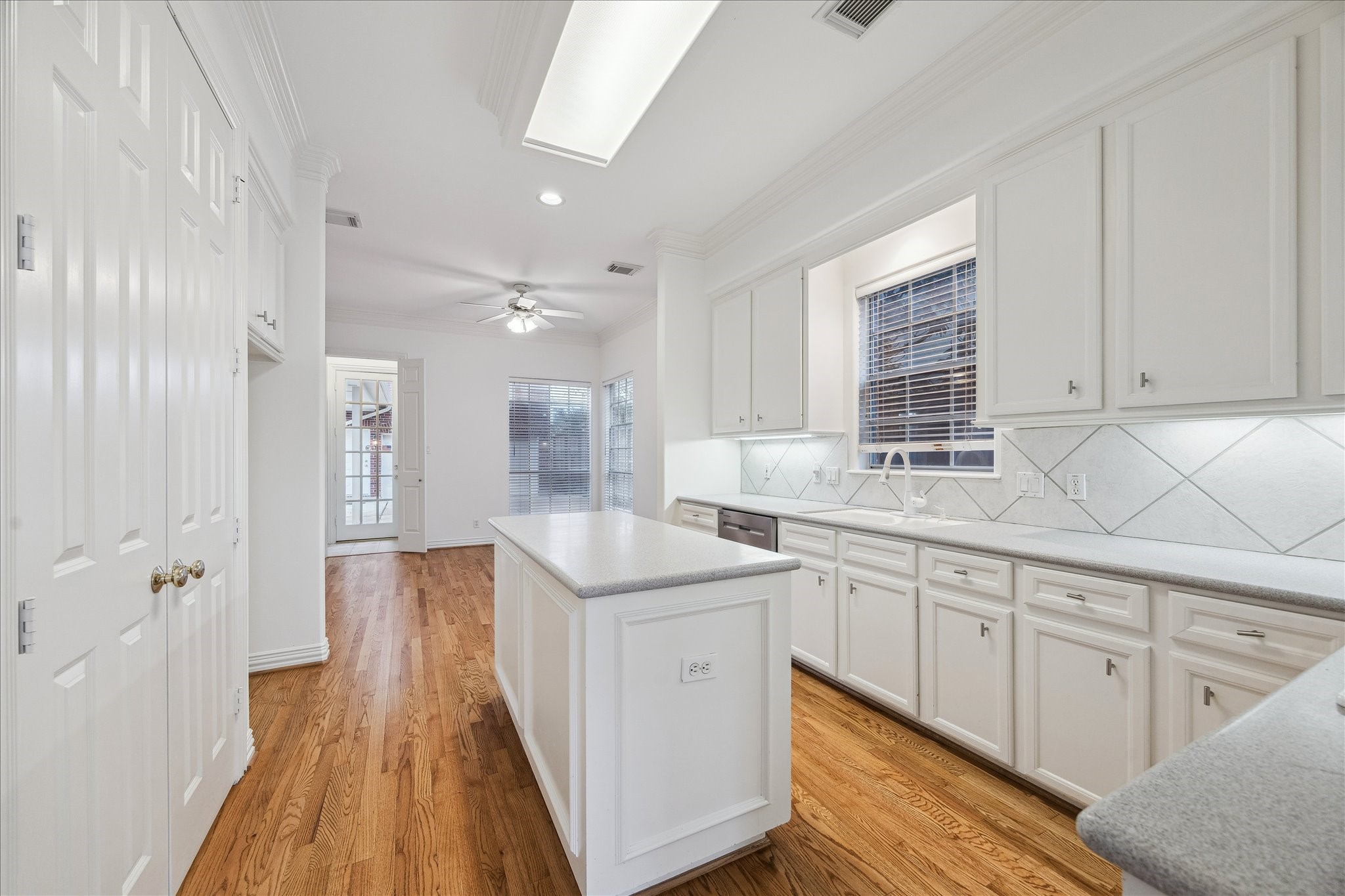 5107 Locust Street Bellaire, TX 77401 - Photo 19 of 45 Bright kitchen featuring white cabinetry, a center island for prep space, stylish tile backsplash, skylight, recessed lighting, & gorgeous hardwood floors, with an open view toward the breakfast area for easy everyday flow.