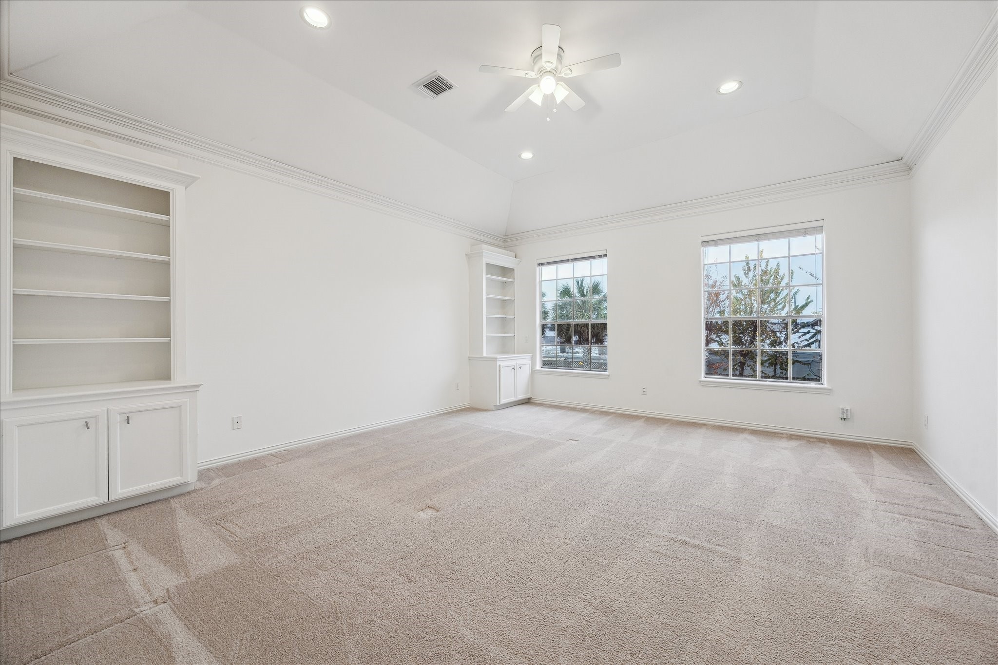 5107 Locust Street Bellaire, TX 77401 - Photo 25 of 45 Spacious primary bedroom featuring plush carpet, crown molding, recessed lighting, a ceiling fan, & large windows that provide natural light. Built-in shelving adds both character and function, creating a serene retreat with space for relaxing or unwinding.