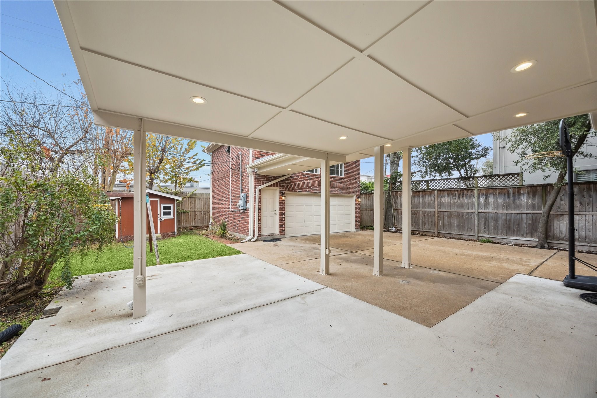 5107 Locust Street Bellaire, TX 77401 - Photo 40 of 45 Expansive covered patio with recessed lighting opens to a wide concrete entertaining area, offering clear views of the detached two-car garage, with apartment, and backyard. The layout provides flexible outdoor space for gatherings, recreation, or everyday enjoyment, with convenient access between the home, patio, and garage.