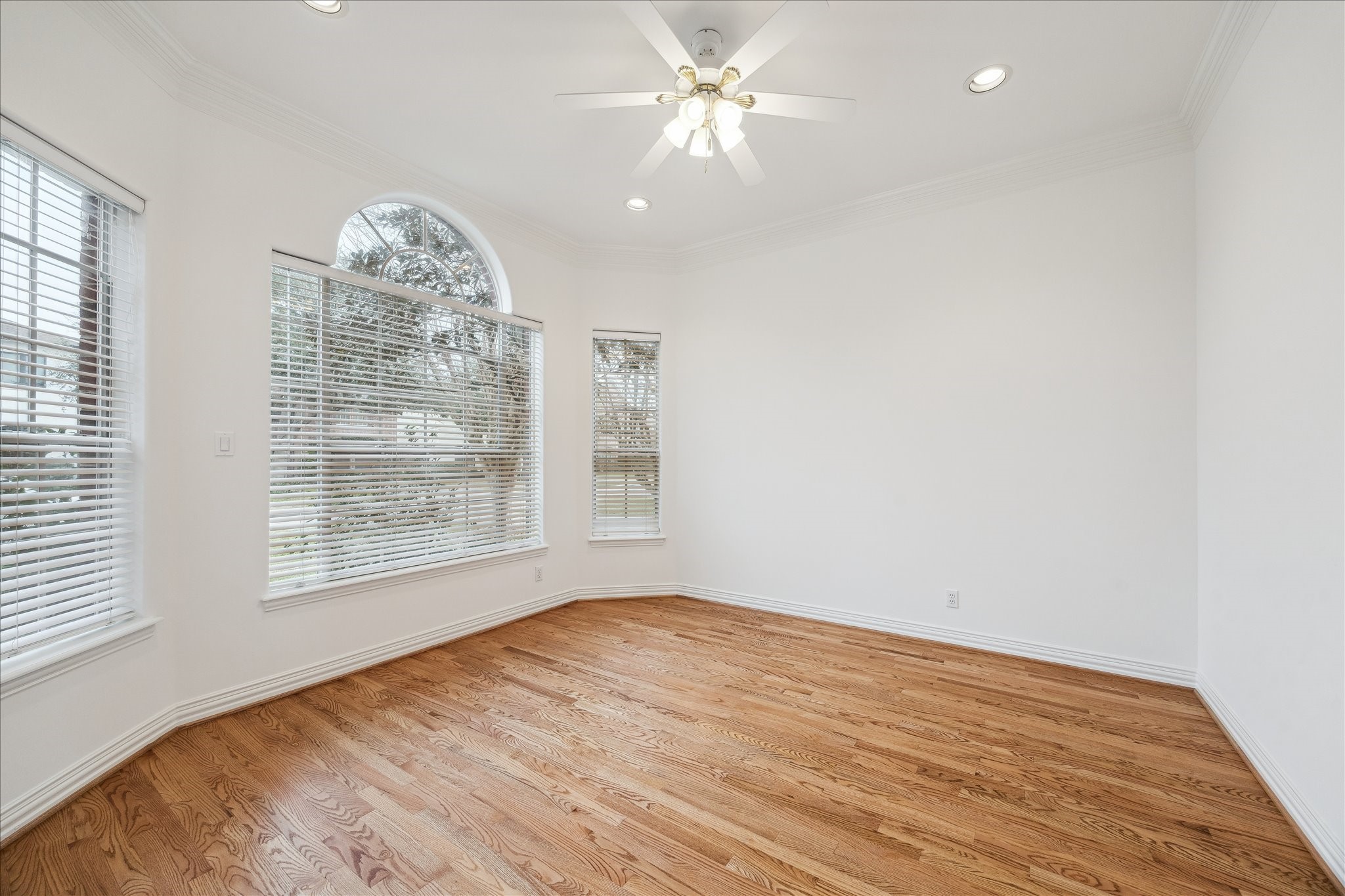 5107 Locust Street Bellaire, TX 77401 - Photo 6 of 45 Front living room featuring hardwood floors, crown molding, recessed lighting, arched windows, & a ceiling fan—an ideal flex space for everyday living, a sitting area, or a secondary workspace.