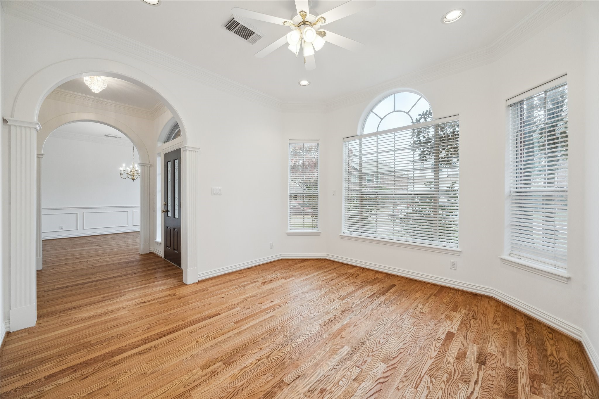 5107 Locust Street Bellaire, TX 77401 - Photo 7 of 45 Additional view of the front living room showcasing hardwood floors, arched windows, crown molding, & recessed lighting, with graceful arched openings that create a seamless flow to the adjacent dining room—well suited for a variety of uses.