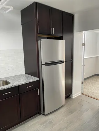 a view of a refrigerator in kitchen and an empty room with wooden floor