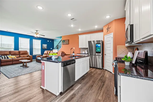 a kitchen with stainless steel appliances granite countertop a stove top oven a sink and a living room view