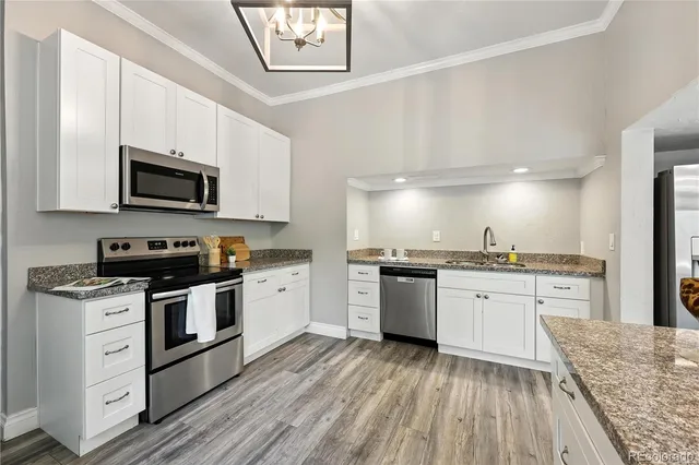 a kitchen with stainless steel appliances granite countertop a stove top oven a sink dishwasher a refrigerator and a dining table with wooden floor