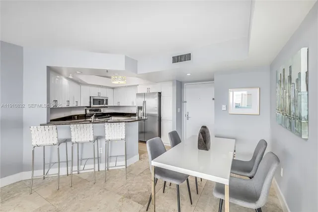 a kitchen with stainless steel appliances kitchen island a table chairs and a refrigerator