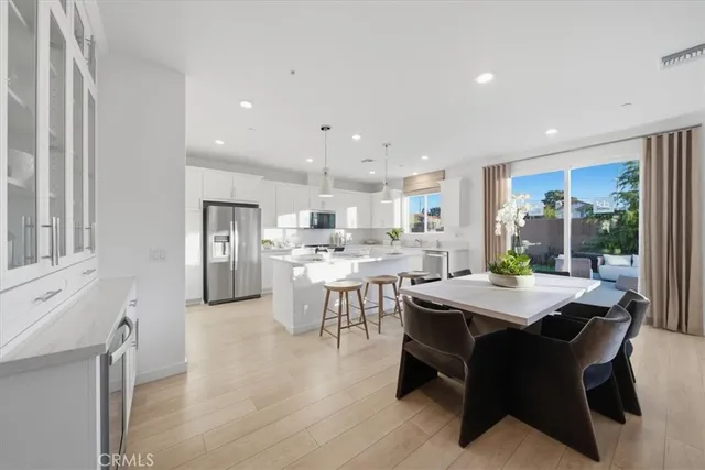 a dining hall with stainless steel appliances kitchen island granite countertop a dining table chairs and a refrigerator