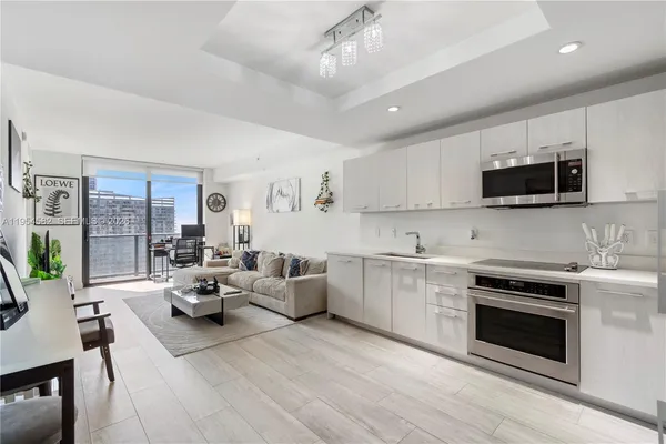 a large white kitchen with stainless steel appliances granite countertop a stove top oven a sink dishwasher a dining table and chairs with wooden floor