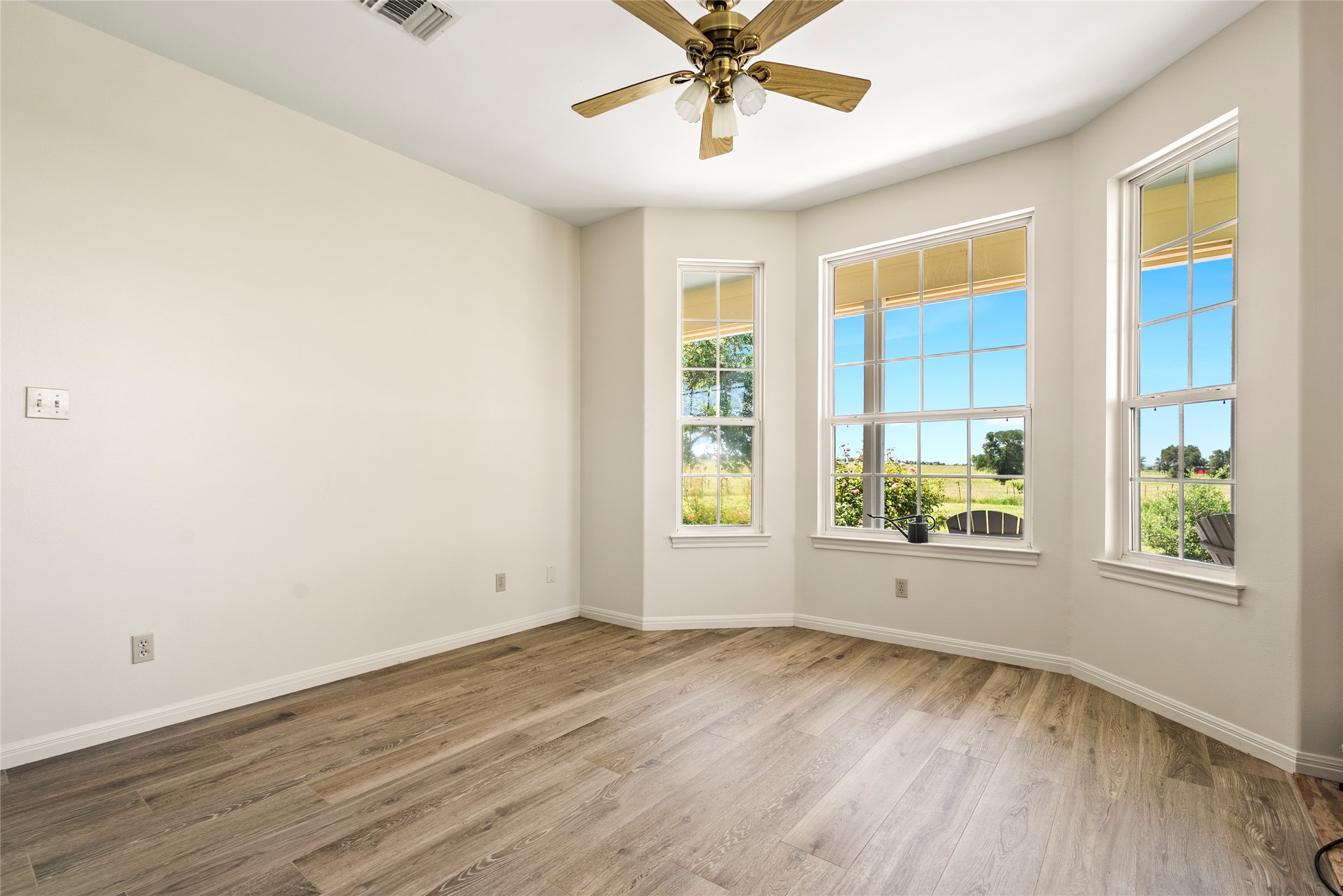 928 Upper Elgin River Road Elgin, TX 78621 - Photo 18 of 40 Room featuring wood-finish flooring, a contemporary ceiling fan, and multiple windows with white trim.