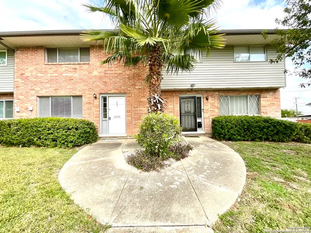 a view of a white house with a small yard plants and large tree