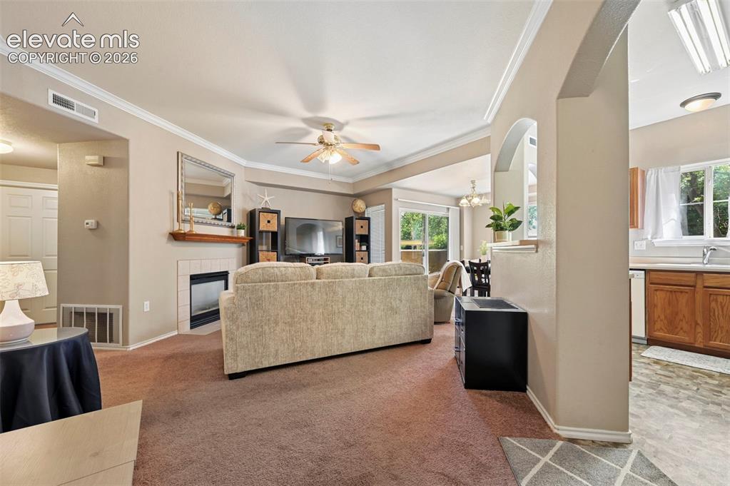 3715 Riviera Grove, Unit 101 Colorado Springs, CO 80922 - Photo 19 of 36 Expansive living area featuring crown molding, a ceiling fan, and a tiled fireplace with a wooden mantle
