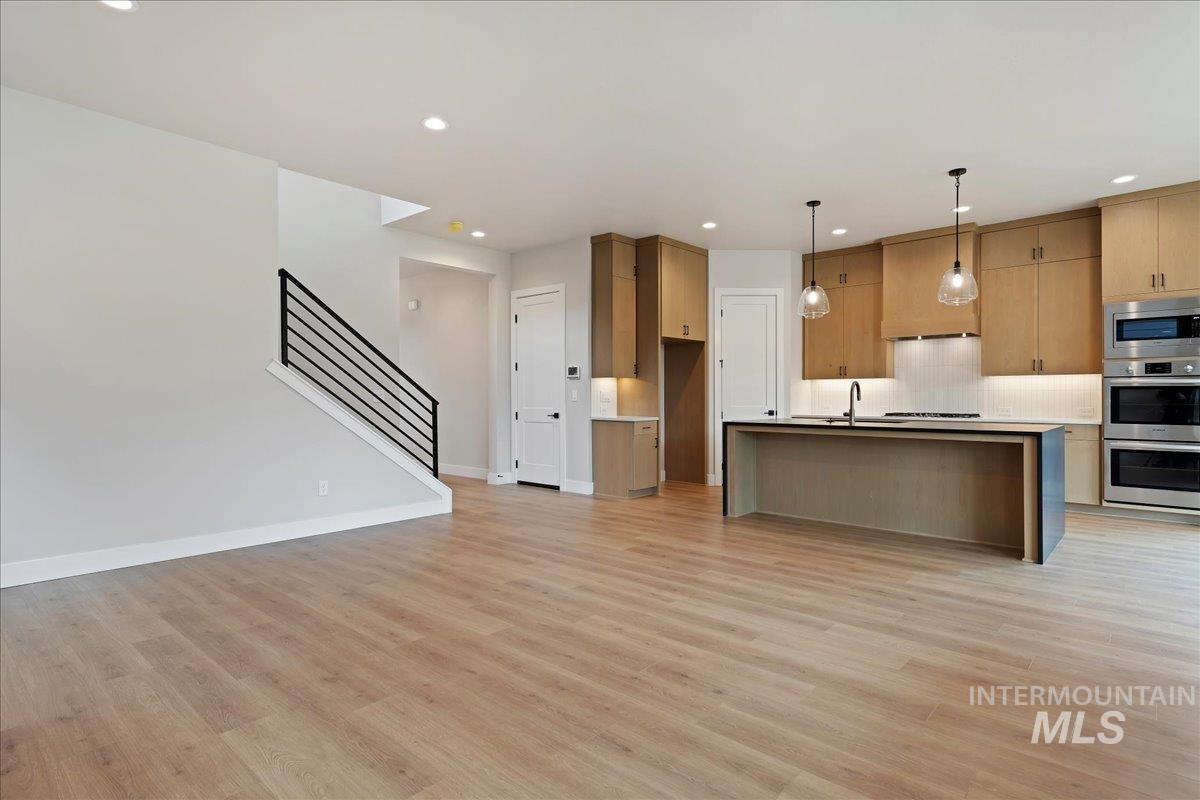 1297 West Malbar Street Meridian, ID 83646 - Photo 12 of 34 Open-concept living area with wood-finish flooring, a modern kitchen island, stainless steel appliances, recessed lighting, and a contemporary staircase with metal railings