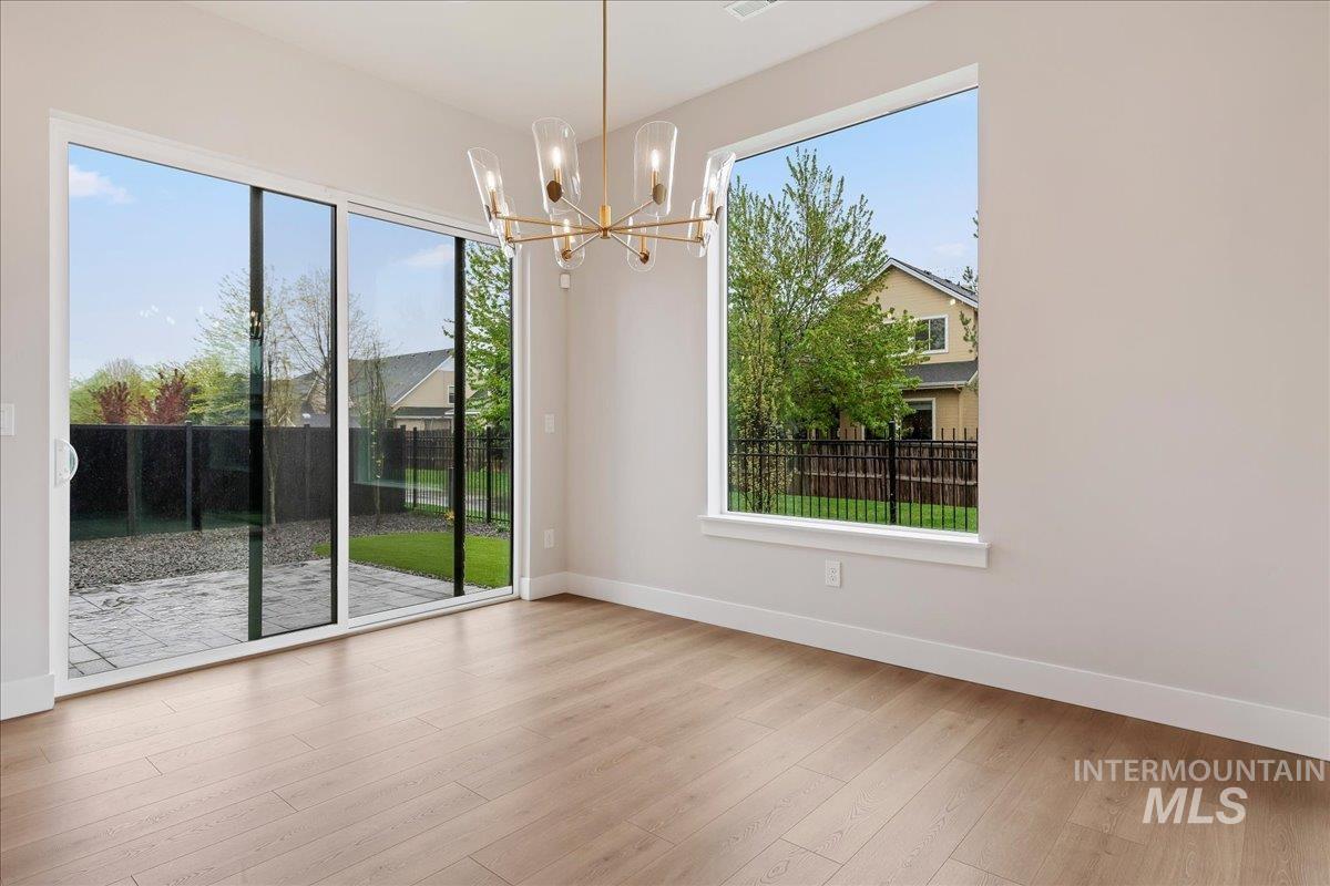 1297 West Malbar Street Meridian, ID 83646 - Photo 14 of 34 Spacious room featuring wood-finish flooring, a contemporary chandelier, large picture window, and sliding glass doors opening to a stone patio and fenced backyard