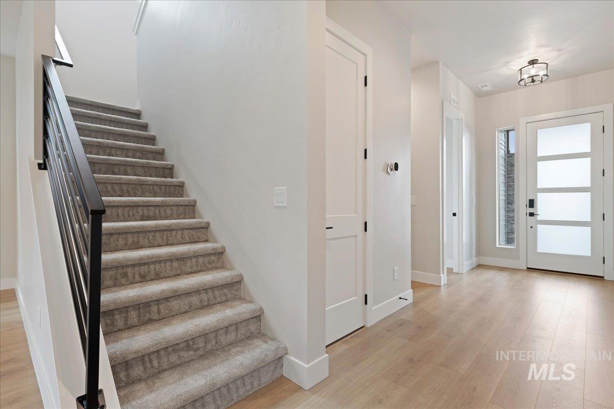 1297 West Malbar Street Meridian, ID 83646 - Photo 17 of 34 Foyer featuring wood-finish flooring, a modern front door with frosted glass panels, a contemporary semi-flush mount light fixture, and a staircase with light-toned carpet and a black metal railing