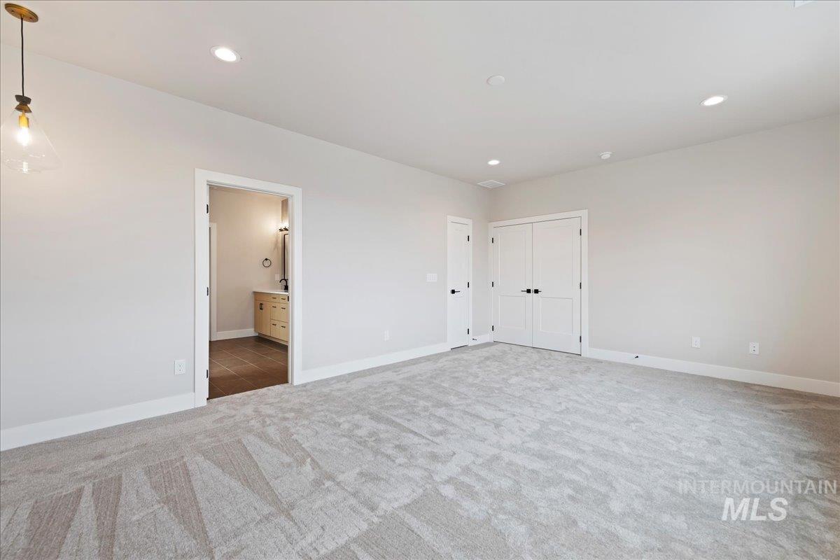 1297 West Malbar Street Meridian, ID 83646 - Photo 20 of 34 Spacious room featuring light gray carpeting, recessed ceiling lighting, a pendant light fixture, and a doorway leading to a bathroom with wood-finish flooring and a vanity