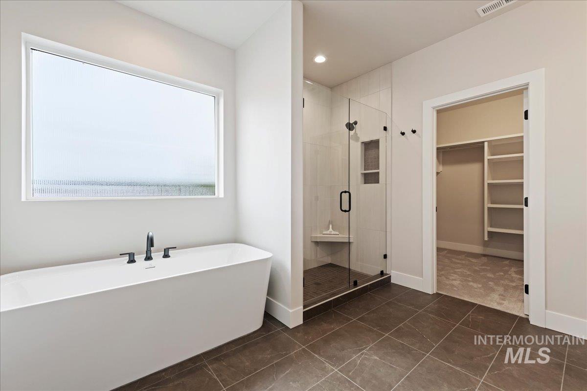 1297 West Malbar Street Meridian, ID 83646 - Photo 22 of 34 Freestanding soaking tub with matte black fixtures, glass-enclosed shower with subway tile surround and built-in bench, and a spacious walk-in closet with shelving