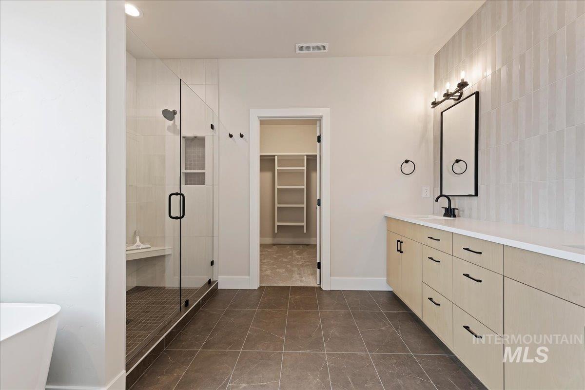 1297 West Malbar Street Meridian, ID 83646 - Photo 24 of 34 Spacious bathroom featuring a frameless glass shower enclosure with a built-in bench, a double vanity with light wood-finish cabinetry and white countertops, a rectangular mirror with matte black frame, and vertical tile accent wall