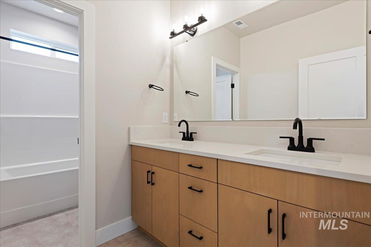 1297 West Malbar Street Meridian, ID 83646 - Photo 30 of 34 Light wood-finish double vanity with integrated sinks, matte black fixtures, full-width mirror, and overhead lighting