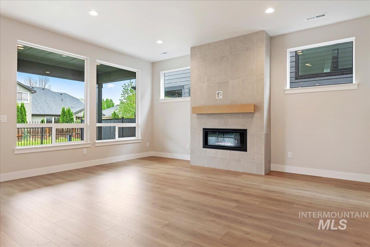 1297 West Malbar Street Meridian, ID 83646 - Photo 10 of 34 Spacious living area featuring light wood-finish flooring, a tiled fireplace with a floating wood mantel, recessed lighting, and multiple large windows