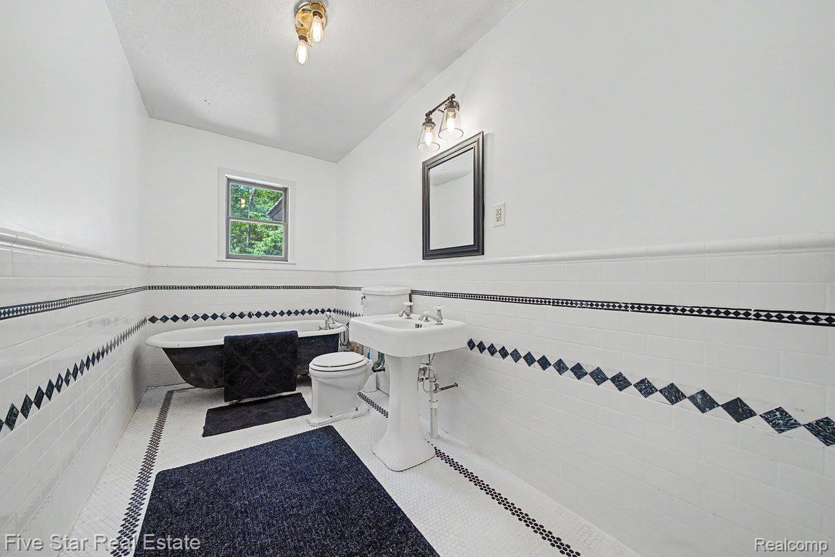 175 Bishop Road Sterling, MI 48659 - Photo 25 of 41 Bathroom featuring a clawfoot tub, pedestal sink, and white subway tile wainscoting with decorative black diamond accents
