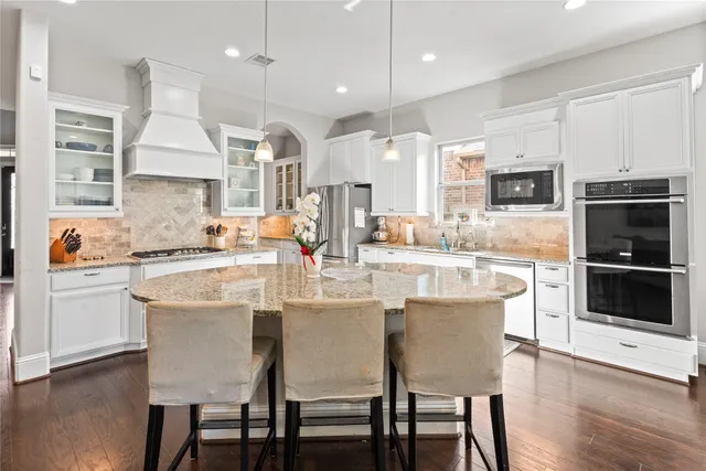 a kitchen with stainless steel appliances granite countertop a sink a stove a refrigerator cabinets and a dining table with wooden floor