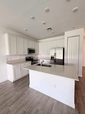 a large kitchen with granite countertop a stove a sink a refrigerator and white cabinets with wooden floor