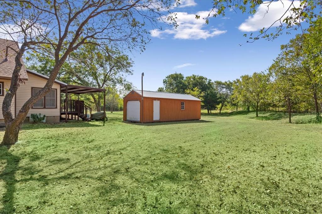 4246 Old Caufield Ranch Road McGregor, TX 76657 - Photo 21 of 31 Expansive lawn area with a detached storage shed, covered porch, and mature trees