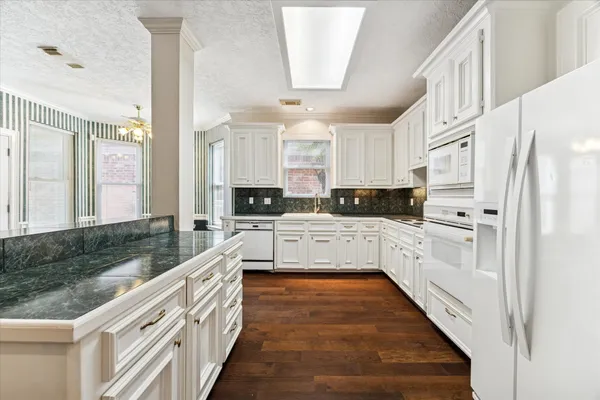 a kitchen with granite countertop a refrigerator sink and white cabinets