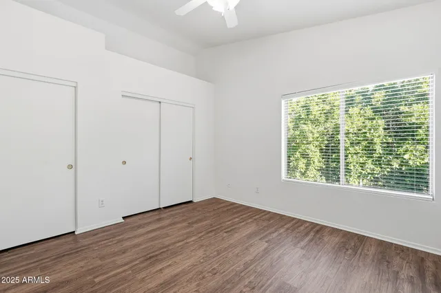 an empty room with wooden floor fan and windows