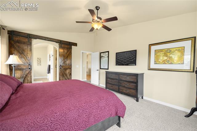 1131 Old North Gate Road Colorado Springs, CO 80921 - Photo 15 of 39 Bedroom with a barn door, lofted ceiling, light carpet, arched walkways, and a ceiling fan