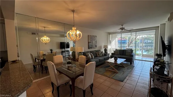 a living room with couches a dining table and a chandelier with kitchen view