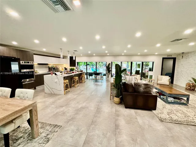 a living room with stainless steel appliances kitchen island granite countertop a table chairs and a refrigerator