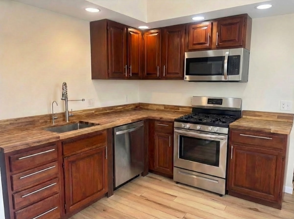 407 Main Street, Unit A Medford, MA 02155 - Photo 3 of 4 a kitchen with stainless steel appliances granite countertop a stove microwave and oven