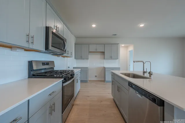 a kitchen with stainless steel appliances granite countertop a sink a stove top oven and white cabinets