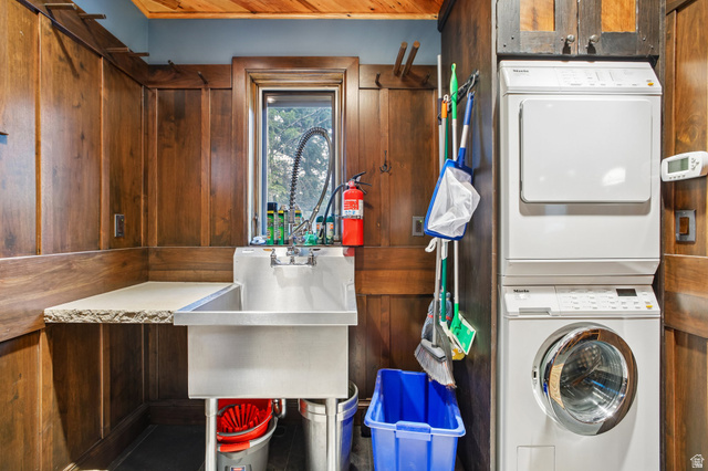 10205 East Moose Loop Road Salt Lake City, UT 84121 - Photo 15 of 50 Utility room featuring wood paneling, a deep stainless steel sink with a gooseneck faucet, a light-colored countertop, and a stacked washer and dryer unit