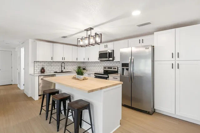 a kitchen with stainless steel appliances a refrigerator a sink dishwasher a stove and white cabinets with wooden floor